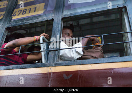 Indischer Mann auf einem Bus ohne Glasfenster und Bars über die Öffnung an der OMR in Kelambakkam unterwegs Stockfoto