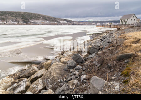 Felsigen Flussufer und schwimmenden Eisbrocken am St.-Lorenz-Strom in Gaspe, Quebec, Kanada. Es gibt weiße große Gebäude und ein d Stockfoto