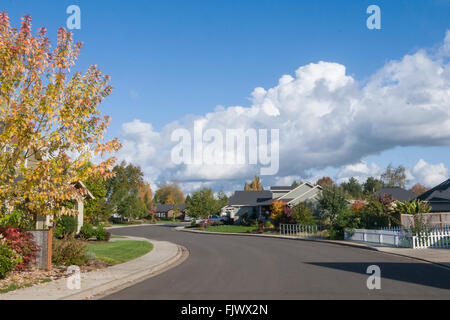 Eine leere Straße biegt aber ein Vorort an einem schönen Herbsttag unter einem strahlend blauen Himmel mit geschwollenen weißen Wolken. Stockfoto