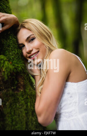 Schöne blonde Frau stand neben einem Baumstamm Stockfoto