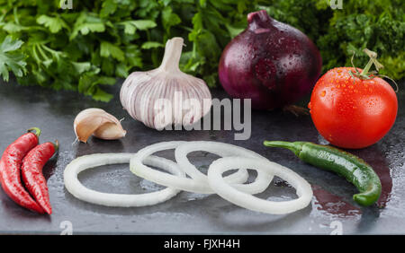 Hot Chili Paprika, Knoblauch, lila Zwiebeln, Fachwerk Tomaten und Petersilie. Rohkost-Zutaten auf Stein Hintergrund nass. Geringe Bautiefe Stockfoto