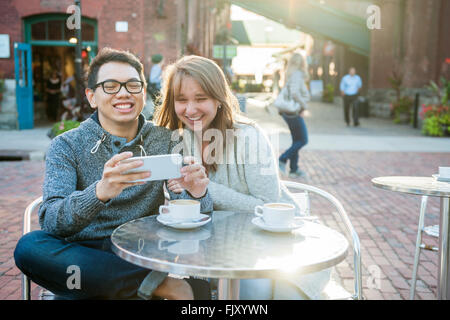 Zwei Jugendliche auf der Suche in Smartphone beim Sitzen an einem Tisch im Café im freien lachen Stockfoto