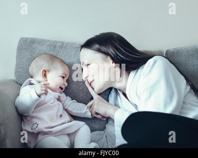 junge Frau mit ihrem Babymädchen auf dem Sofa spielen Stockfoto