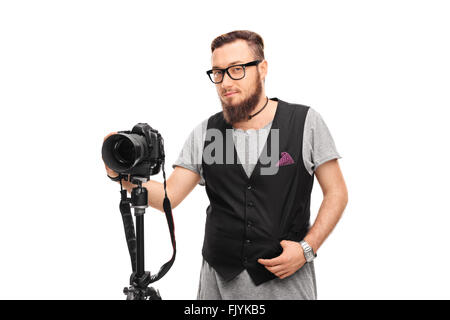 Junge männliche Hipster mit schwarzer Brille und eine schwarze Weste hält eine Kamera isoliert auf weißem Hintergrund Stockfoto