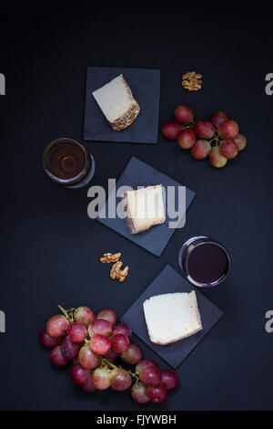 Käsestücke auf schwarzem Hintergrund, begleitet von Wein, Sherry und Walnüssen Stockfoto