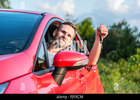 Mann sitzt In einem Auto zeigt neue Fahrzeugschlüssel. Stockfoto