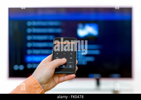 Nahaufnahme auf Frau Hand mit Smartphone und Nutzung einer app mit Fernbedienung und Surfen Programme im Fernsehen. Stockfoto