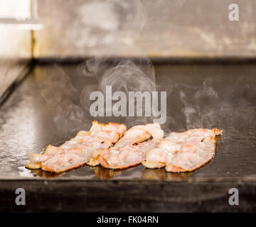 Nahaufnahme von lecker gebratene Speckstreifen auf Grillen Panel. Lecker gekocht Speck Speckscheiben Nahaufnahme, Speck braten, Grill oder Barbecue Stockfoto