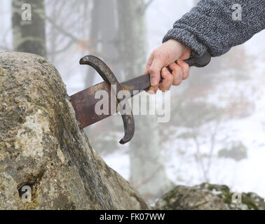 Hand des tapferen Ritters versucht, das magische Schwert Excalibur in den Stein zu entfernen Stockfoto