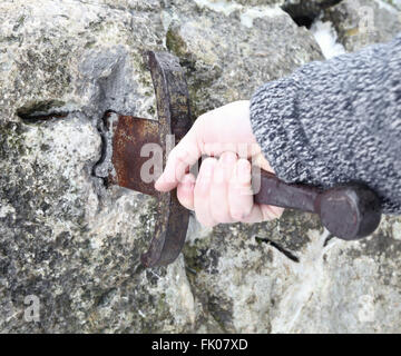 Hand des tapferen Ritters versucht, das magische Schwert Excalibur in den Stein zu entfernen Stockfoto