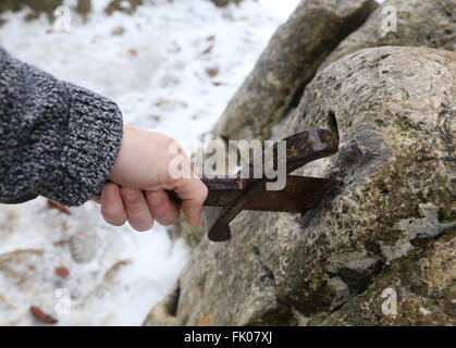 Hand des tapferen Ritters versucht, das magische Schwert Excalibur in den Stein zu entfernen Stockfoto