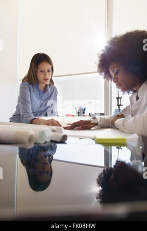 Team von zwei weiblichen Architekten, sitzen am Schreibtisch im Büro. Die Frauen reden, einen Bauplan zu überprüfen. Reflexionen über Tisch und cop Stockfoto
