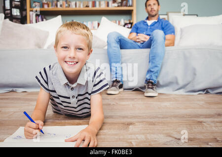 Porträt des jungen Zeichnung in Buch während Vater auf sofa Stockfoto