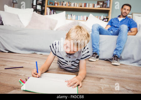 Junge, die Zeichnung im Buch während Vater auf sofa Stockfoto