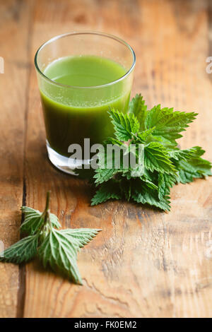 Brennnesselblätter und ein Glas frischen Brennnesselsaft auf Holztisch. Stockfoto