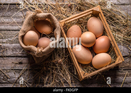 Haufen von frischen braunen Eiern in einer Holzkiste und im Leinensack Stockfoto