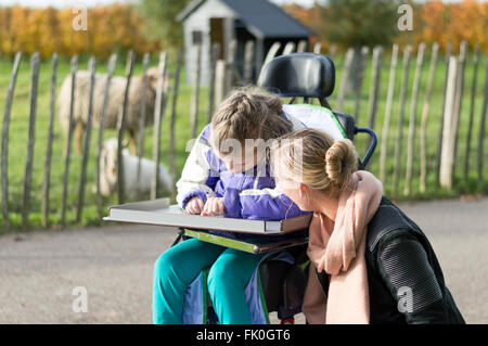 Ein behindertes Kind im Rollstuhl entspannend außerhalb mit einem freiwilligen Pflegedienst Stockfoto