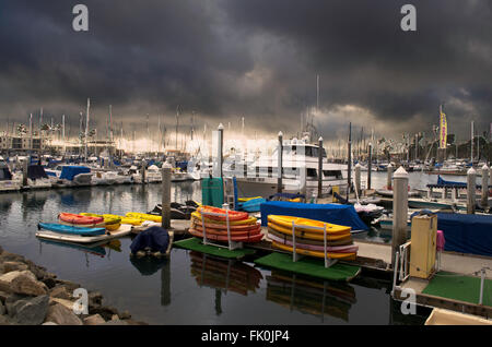 Gewitterwolken über Hafen, Boote angedockt, bunte Boote und Kajaks auf Dock gestapelt. Stockfoto