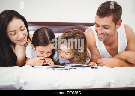 Glückliche Kinder Buch mit Eltern auf Bett Stockfoto