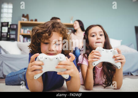 Geschwister mit Controller spielen Videospiel auf Teppich zu Hause Stockfoto