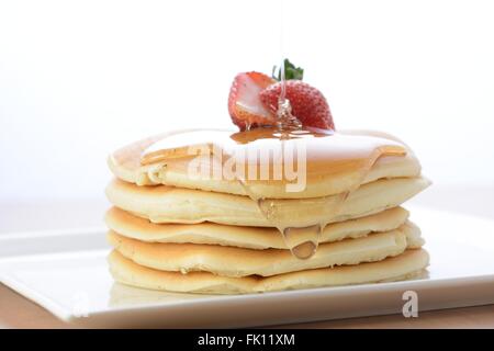 Stapel mit leckeren Pfannkuchen mit Honig auf Platte isoliert auf weiss Stockfoto