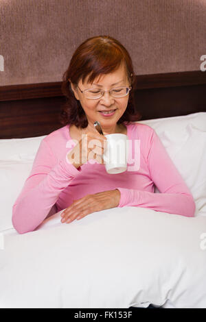 Asiatische Senior mit Tee im Bett entspannen. Stockfoto