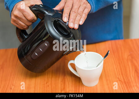 Gießen heißes Wasser aus der Flasche in Tasse. Stockfoto
