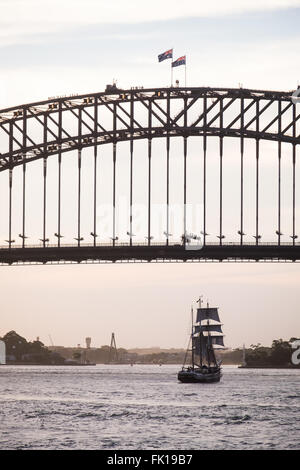 Ein altes Segelschiff unterquert die Sydney Harbour Bridge Stockfoto