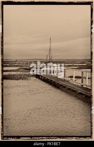 Sepia monochrome Film umrahmt Szene Holzstege durch Salzwiesen, die Zugriff auf die Schlamm-Liegeplätze in Tollesbury Marina Essex UK Stockfoto