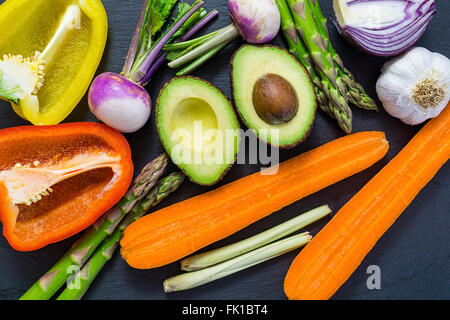 In Scheiben geschnitten frisches Gemüse auf einem dunklen Brett, Draufsicht, Rundweg, Avocado, Paprika, Zwiebel Stockfoto