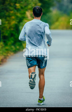 männlicher Athlet läuft im Park eine asphaltierte Straße. Blick vom Rücken in ein Sweat-shirt Stockfoto