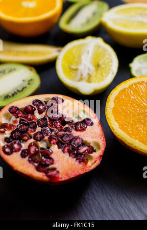 Nahaufnahme auf einem dunklen Brett mit geschnittenem Obst, Lime, Orange, Zitrone, Banane, Granatapfel Stockfoto