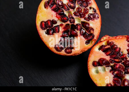 Granatapfel-Frucht in Scheiben geschnitten in der Mitte, auf einem dunklen Brett flach Stockfoto