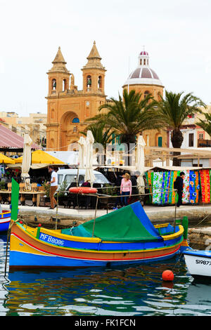 Traditionelle maltesische Luzzu Angelboote/Fischerboote im Hafen von Marsaxlokk mit Kirche der Muttergottes von Pompeji hinter Marsaxlokk, Malta. Stockfoto