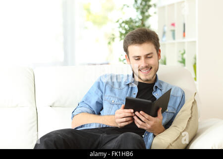 Glücklicher Mann ein Buch in ein Ebook-Reader sitzt auf einer Couch zu Hause Stockfoto