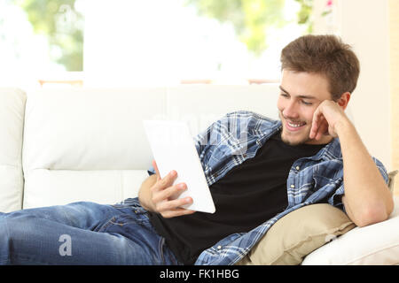 Mann liest ein Ebook oder Tablet sitzt auf einer bequemen Couch zu Hause Stockfoto