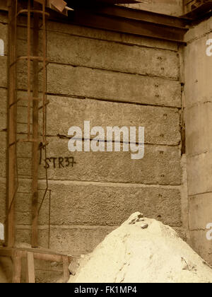 Die Industrieruinen. Ein Haufen Sand, Leiter mit Sicherheitsbarriere und lustige Graffiti auf den Tellern Stockfoto