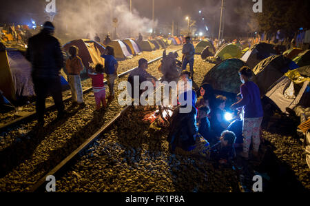 Idomeni, Griechenland. 5. März 2015. Flüchtlinge sitzen auf Bahnschienen durch ein Lagerfeuer vor ihren Zelten im Flüchtlingslager an der griechisch-mazedonischen Grenze in Idomeni, Griechenland, 5. März 2015. Nur wenige Flüchtlinge aus Syrien und dem Irak werden über die Grenze nach Mazedonien jeden Tag vermietet werden. Foto: KAY NIETFELD/Dpa/Alamy Live News Stockfoto