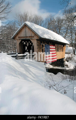 Überdachte Brücke nach Schneefall zeigt Patriotismus mit amerikanischer Flagge über die Seite in Neu-england drapiert. Stockfoto