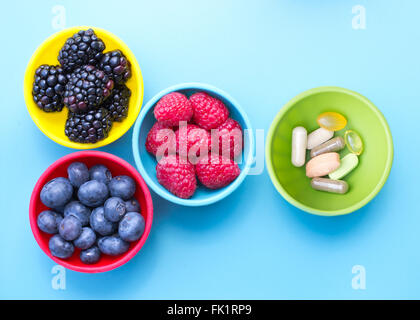 Beeren und Nahrungsergänzungsmittel in bunten Schalen von oben auf die blaue Fläche betrachtet Stockfoto