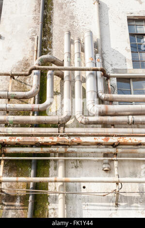 Alte Rohre an der Wand außerhalb einer alten verlassenen Fabrik. Stockfoto