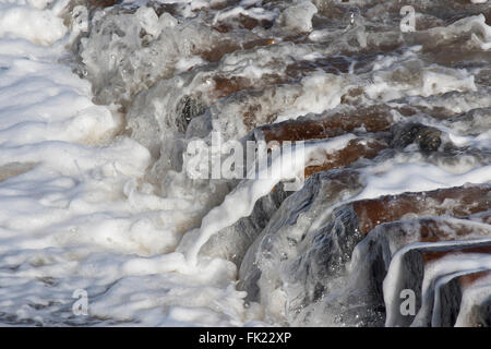 Breaking Waves über Holz und Stein Felsen Rüstung Buhnen. Stockfoto