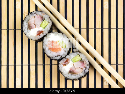 Drei Sushi-Rollen und Stäbchen über Bambusmatte Stockfoto