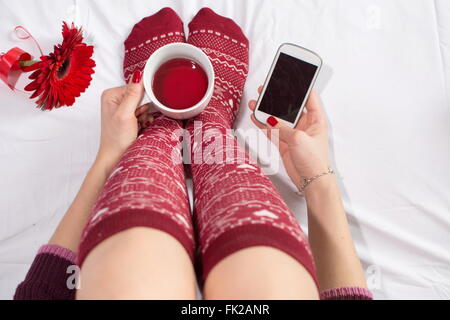 Frau mit einer Tasse Tee und SMS im Bett Stockfoto