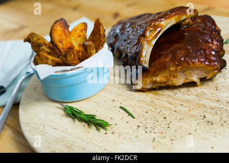 Rauchige Grill Ribs mit Kartoffelspalten, Kräuter und Gewürze auf einem Holztablett Stockfoto