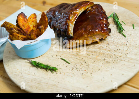 Grillen Sie Schweinerippchen mit Sauce, Kartoffeln und Gewürze auf einem Holztablett und Kräutern, bereit um zu essen Stockfoto