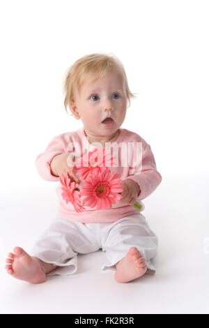 Baby Mädchen ist sitzen auf dem Boden mit rosa Blüten auf weißem Hintergrund Stockfoto
