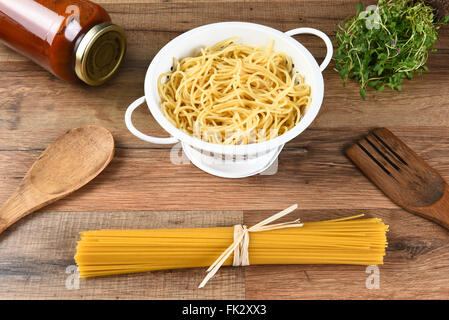 Stillleben mit getrockneten Spaghetti, gekochte Nudeln in ein Sieb geben, ein Glas mit Soße, Kräutern und Holz Utensilien. Stockfoto