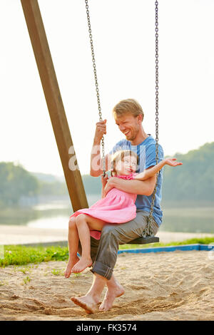 Vater und Tochter gemeinsam schwingen auf einer Schaukel auf einem Spielplatz im Sommer Stockfoto