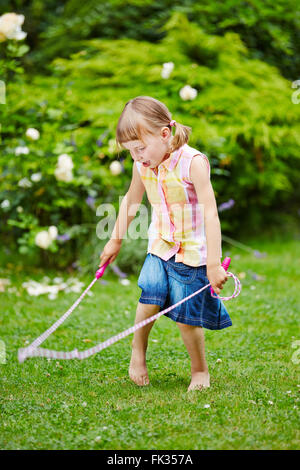 Mädchen spielen mit Springseil im Garten im Sommer Stockfoto